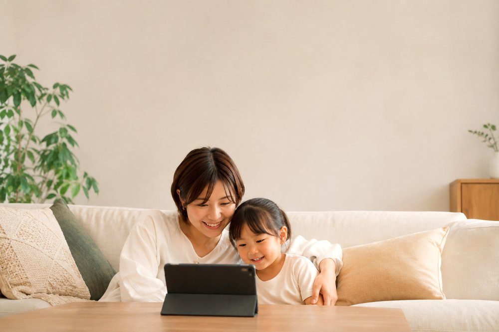 リビングのソファでタブレットのレッスンを一緒に見る親子